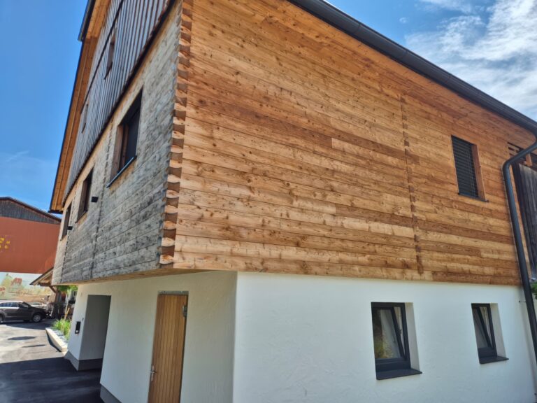 Fassade aus naturbelassener Lärche mit gehackter und gebürsteter Blockwandschalung, traditioneller Klingschrotverbindung und sägerauer Lärchenschalung im steirischen Stil.