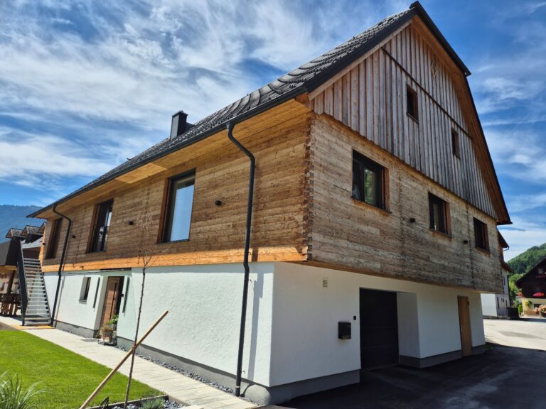 Fassade aus naturbelassener Lärche mit gehackter und gebürsteter Blockwandschalung, traditioneller Klingschrotverbindung und sägerauer Lärchenschalung im steirischen Stil.