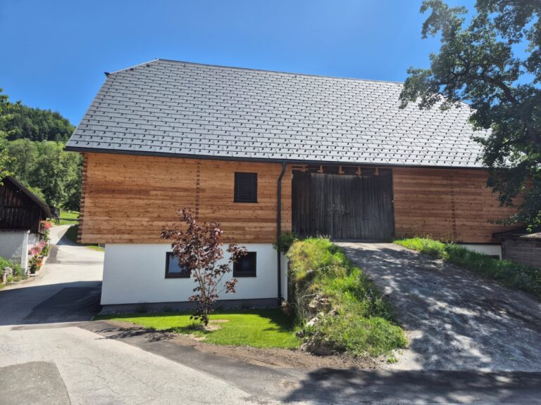 Fassade aus naturbelassener Lärche mit gehackter und gebürsteter Blockwandschalung, traditioneller Klingschrotverbindung und sägerauer Lärchenschalung im steirischen Stil.